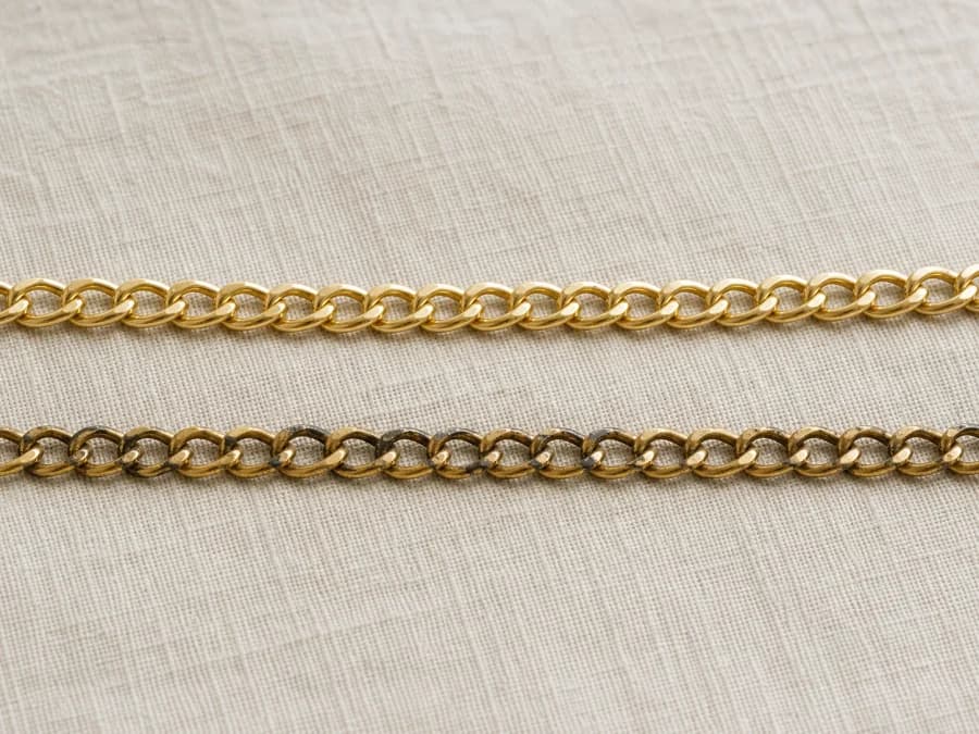 Bright new gold-tone chain beside a worn chain with dulled patches on linen