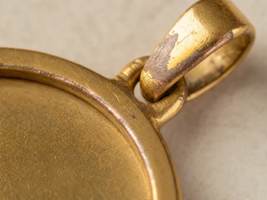 Macro view of a gold-plated pendant edge where the coating has worn to darker base metal